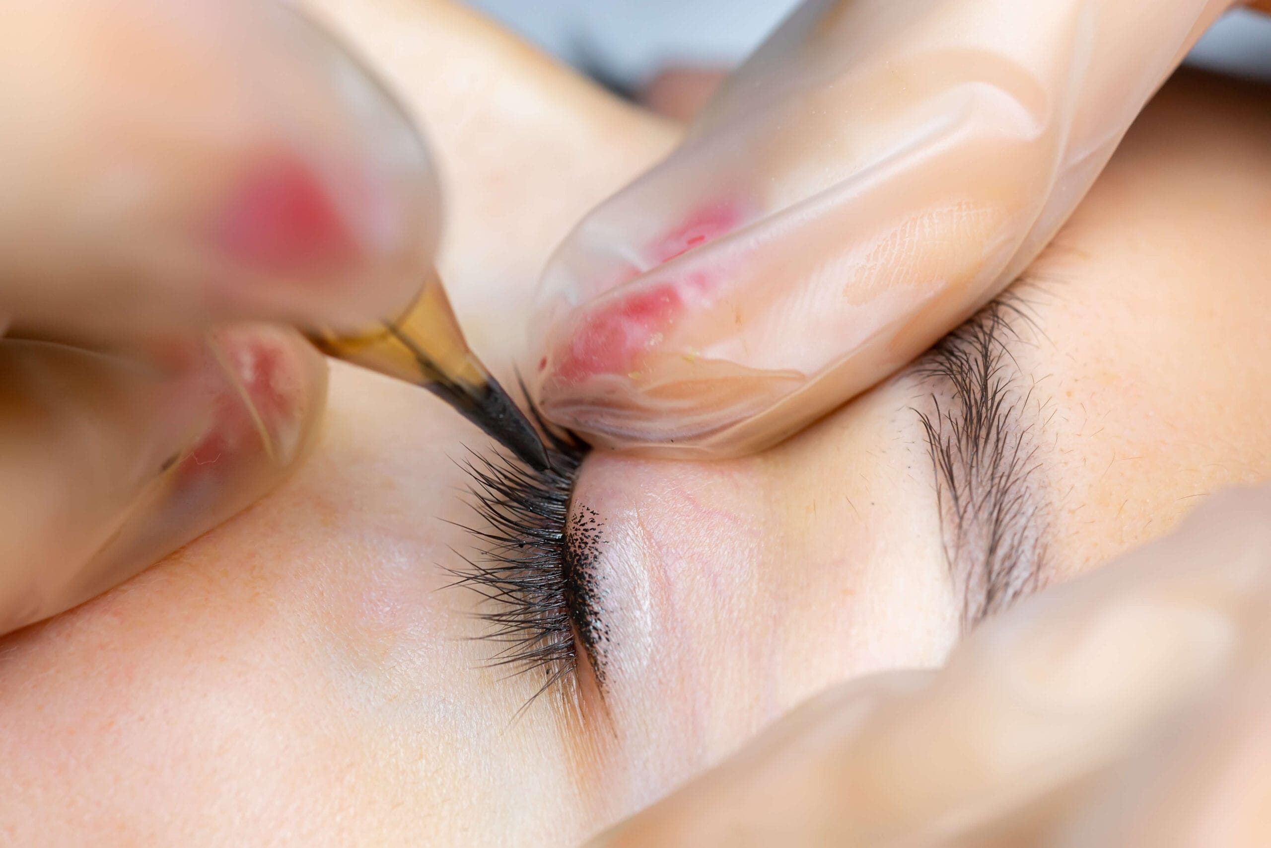 Micropigmentación ojos sombra Tratamiento de micropigmentación de delineado de ojos con dermógrafo en Rocío Martín Micropigmentación y Estética; mano enguantada en rosa aplicando pigmento con precisión sobre el párpado
