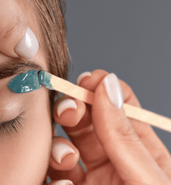 Aplicación detallada de cera tibia en la zona de las cejas para depilación, realizada por profesional en Rocío Martín Micropigmentación y Estética Madrid; técnica precisa y segura que define la forma natural de las cejas y cuida la piel sensible del rostro